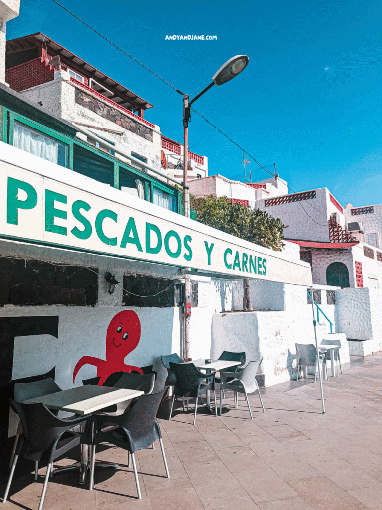A seafood and meat restaurant with outdoor seating, featuring a playful octopus mural and a clear blue sky in Las Playitas, Fuerteventura.