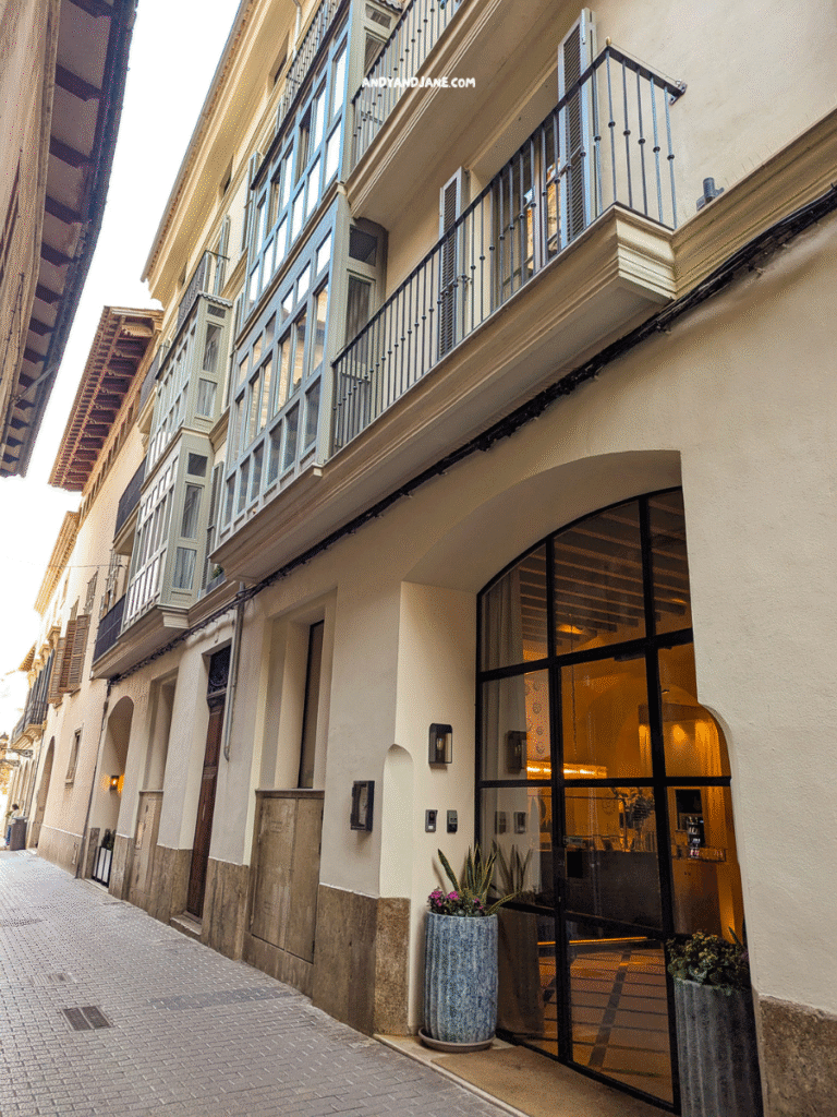 A narrow street view of Hotel Basilica with balconies and glass doors, leading to a welcoming hotel entrance.