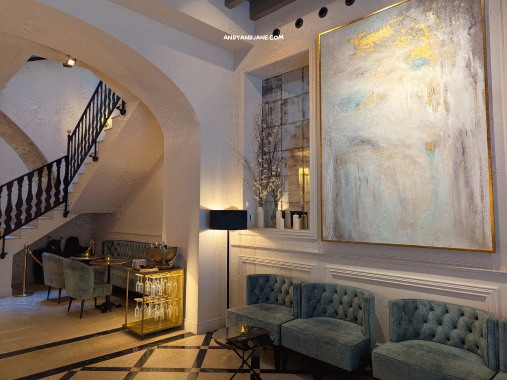 Luxurious lobby at Hotel Basilica with a large abstract painting, plush teal seating, and a stylish bar cart, highlighted by warm lighting.