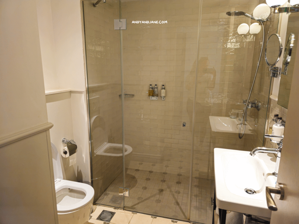A modern bathroom featuring a glass shower, toilet, and sink with stylish fixtures, accented by light-colored tiles.