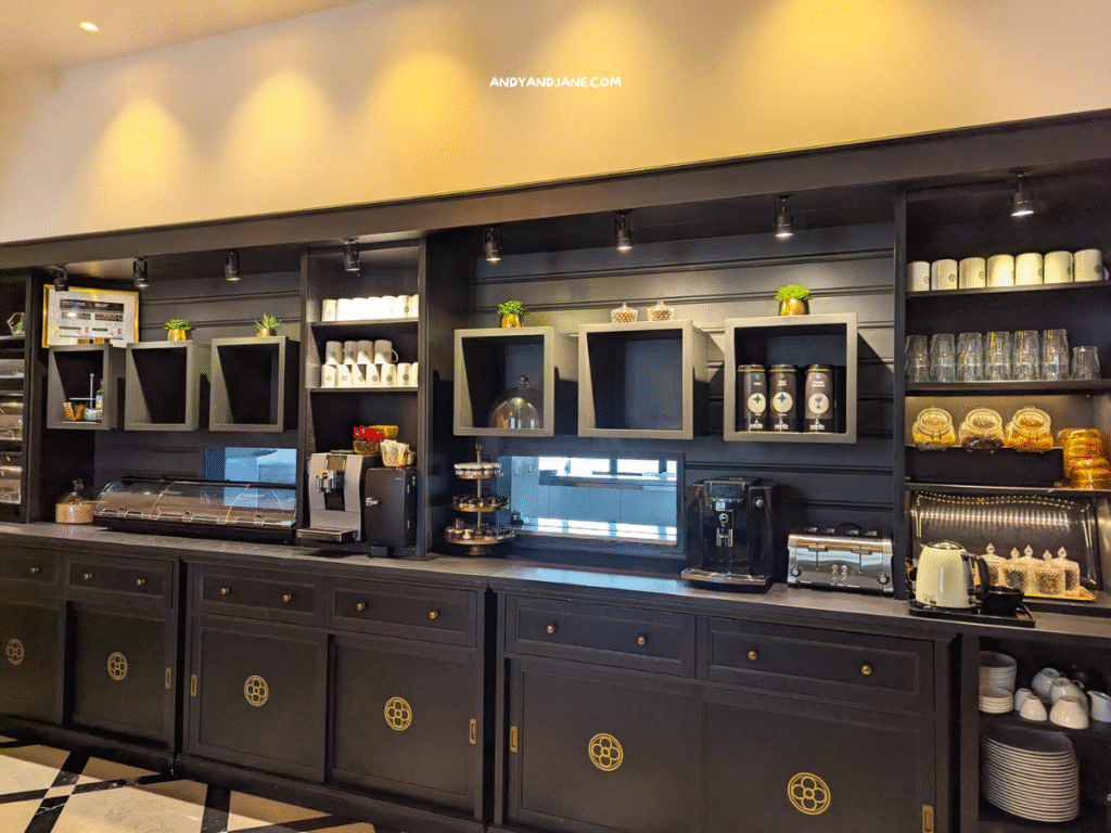 Breakfast area at Hotel Basilica featuring black cabinetry, coffee machines, cups, and pastries, accented with small plants and warm lighting.
