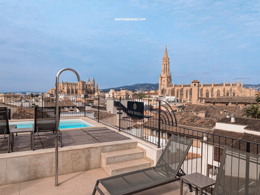 Rooftop pool area at Hotel Basilica with lounge chairs overlooking a picturesque cityscape, featuring a stunning gothic cathedral of Palma in the background.