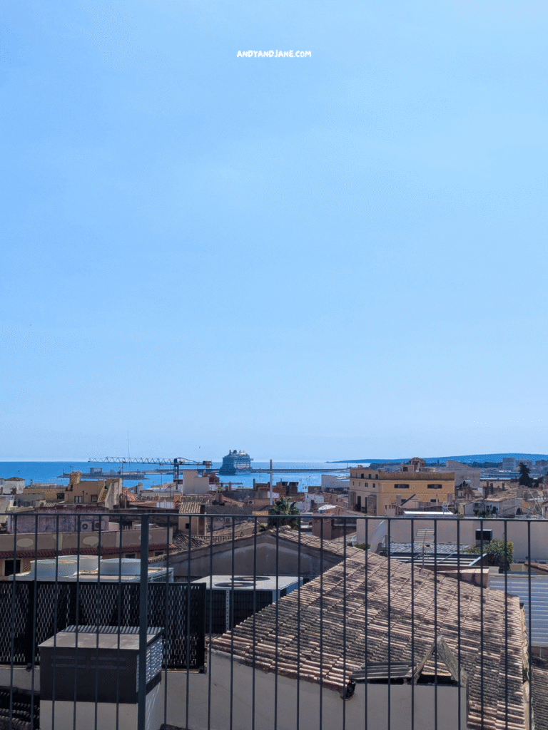 A panoramic view of a Palma from Hotel Basilica, featuring rooftops, a distant ship, and a clear blue sky.