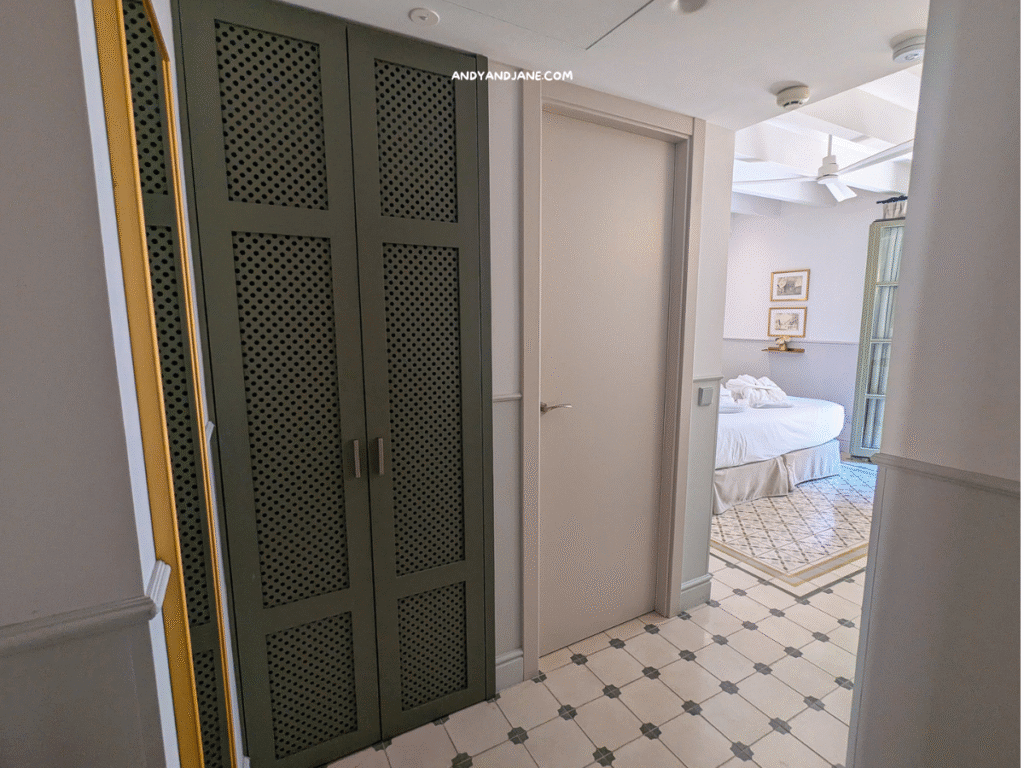 A stylish hallway leading to the bedroom at Hotel Basilica, featuring green mesh cabinets, a neutral door, and patterned tile flooring.