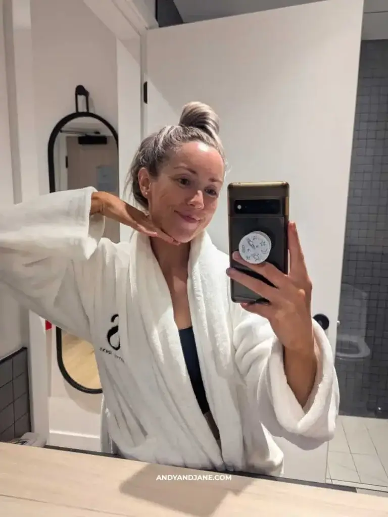 A person in a white bathrobe takes a selfie in a stylish bathroom, showcasing a mirror and modern decor.