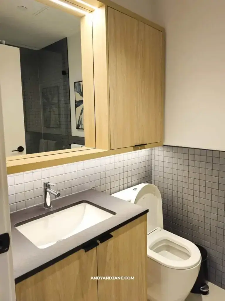 Modern bathroom with wood cabinets, a square sink, and a sleek toilet. Gray tile backsplash enhances the minimalist design, conveying a clean and calm ambiance.