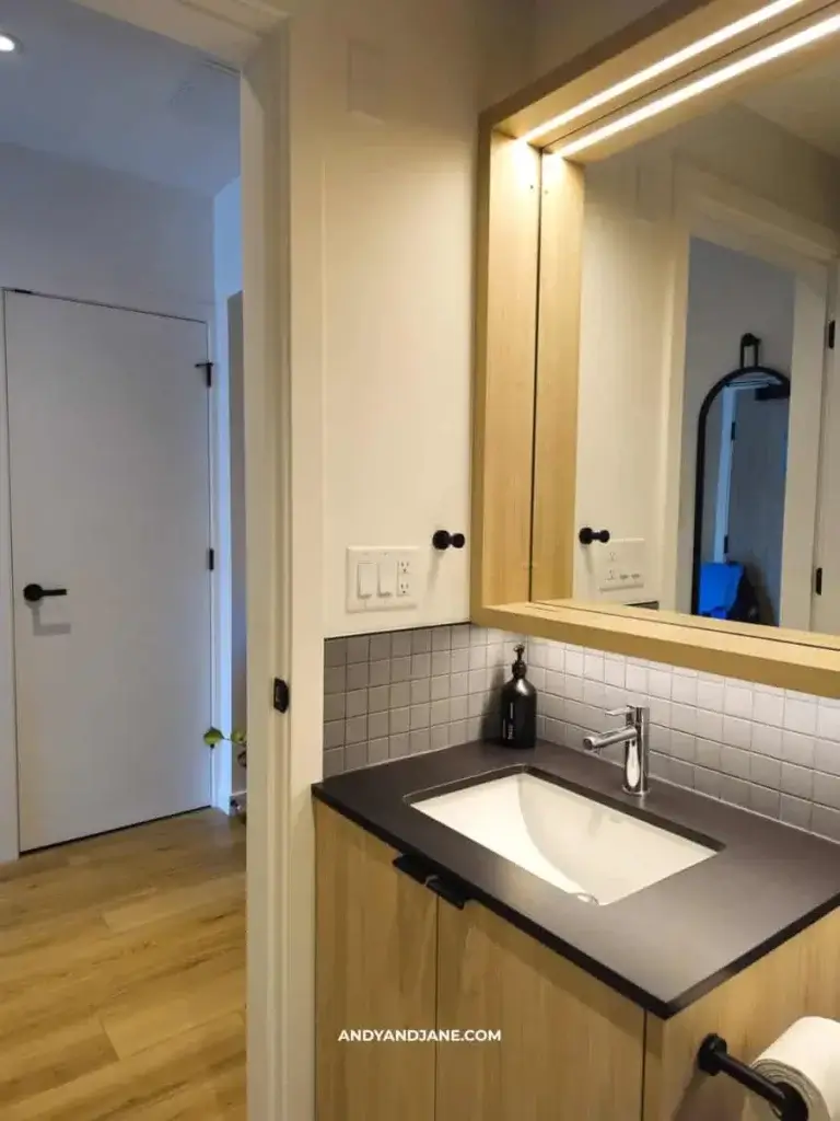 Modern bathroom with a sleek black countertop, square sink, and wall-mounted faucet. Light wood vanity and large mirror create a minimalist look.