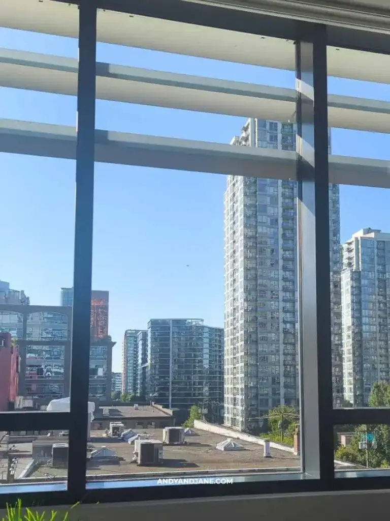 View of modern urban buildings through large window panes, with a clear blue sky above.